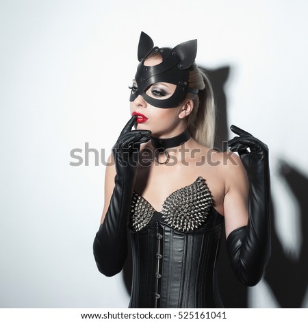 Beautiful dominant blonde vamp mistress girl in leather corset, gloves, collar and bdsm black leather fetish cat mask posing on white backgroung