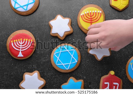 Female hand taking tasty glazed cookie for Hanukkah from dark grunge table