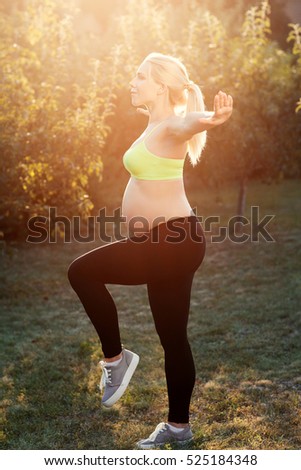 Pregnant woman practicing yoga early in morning. Side view on expectant female holding balance, sun light flare. Relaxation, health and body care, peacefulness, strong body, healthy pregnancy concept