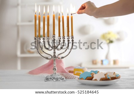 Female hand applying match to candles in menorah on wooden table. Hanukkah concept