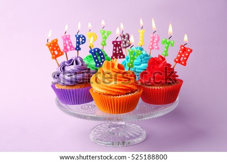 Tasty colorful cupcakes with Happy Birthday candles and glass stand on color background