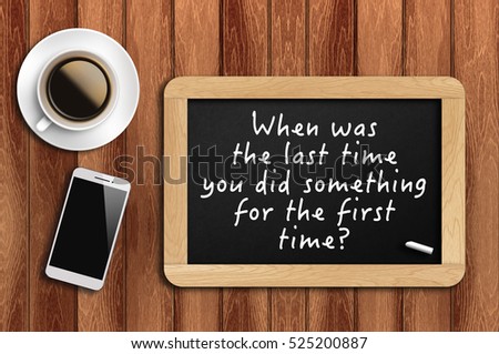 Inspirational motivating quote on chalkboard with coffee, phone and wooden background. When was the last time you did something for the first time?