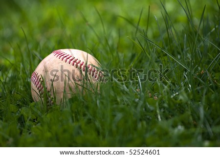 One aged and worn hardball or baseball laying in the green grass.