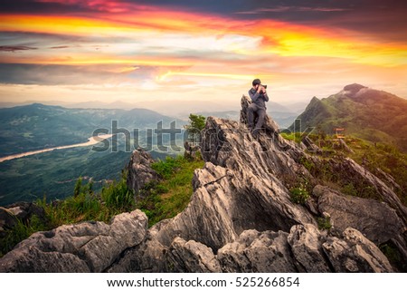 Professional photographer takes photos on the peak of rocks mountain at sunset, success,winner, leadership concept