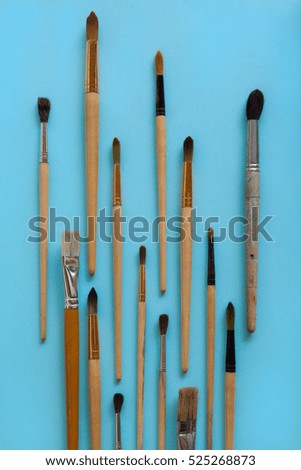A lot of different sizes brushes for painting on bright blue paper background. Drawing education and inspiration concept.