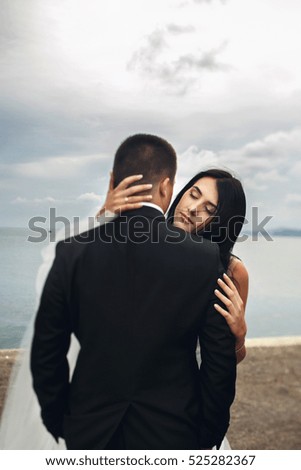 Look from behind groom's back at bride hugging him tender on the harbor