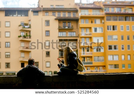 Couple sits on the wall over the river looking at yellow buildings