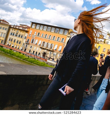 Wind blows girl's red hair while she walks over the bridge