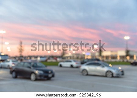 Blurred image exterior view of modern shopping center in Humble, Texas, US at sunset. Mall complex with row of cars in outdoor uncovered parking lots and bokeh light of retail store in background.
