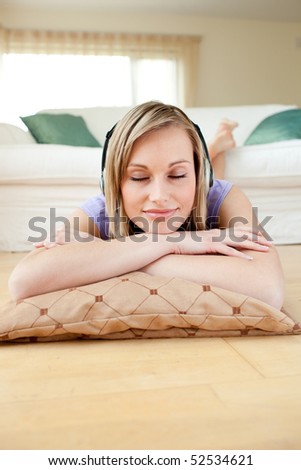Beautiful woman listening music with headphones lying on the floor