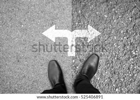 Businessman in black shoes standing at the crossroad making decision which way to go - easy or hard Royalty-Free Stock Photo #525406891