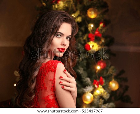 Christmas manicure. Beautiful smiling woman portrait. Makeup. Healthy long hair style. Elegant lady in red dress over christmas tree lights background. Xmas Gifts.