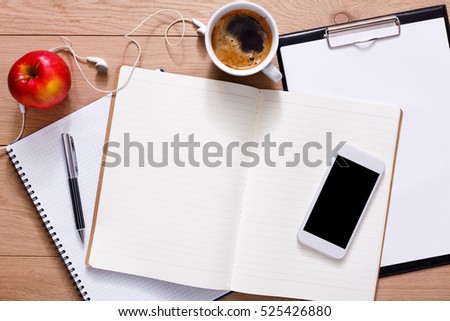 Notepad, diary and mobile with espresso coffee. Office supplies and business devices on modern wooden office desk. Working table top view. Education or job background with copy space on paper sheet