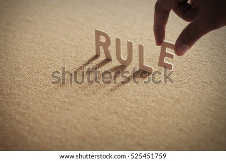RULE wood word on compressed board with human's finger at E letter