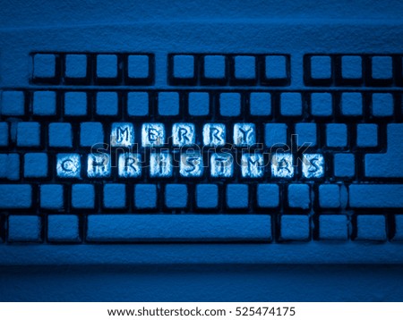 keyboard covered with snow with words Merry Christmas illuminated with blue light
