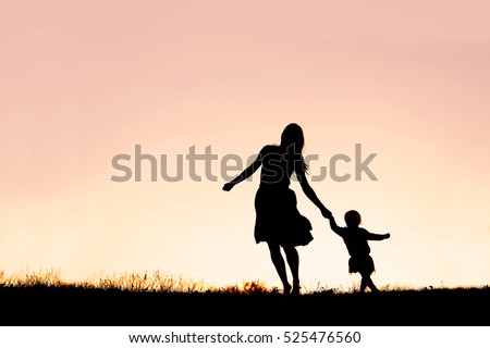 Silhouette of a happy mother and her baby daughter holding hands, and running and dancing outside at sunset.