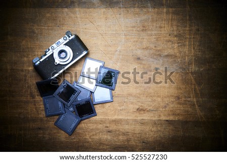 Vintage photo camera with slides on a scratched old wooden table. Focused to camera.