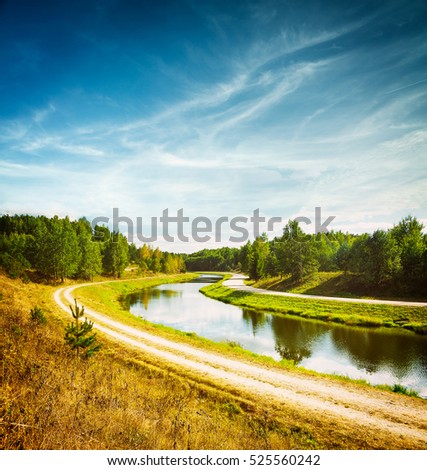 Summer Landscape with River and White Clouds at Blue Sky. Beautiful Non Urban Scenery. Road near the River. Scenic Nature Background. Toned and Filtered Photo with Copy Space.