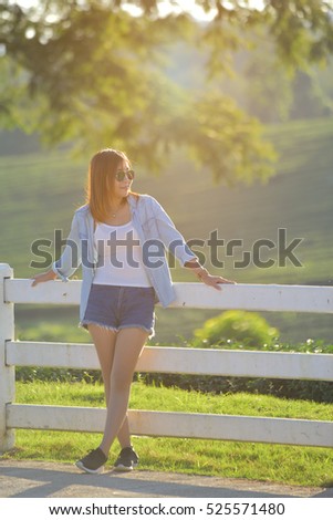 Young asian woman dress in casual and jeans,standing by a fence on a ranch in warm toned