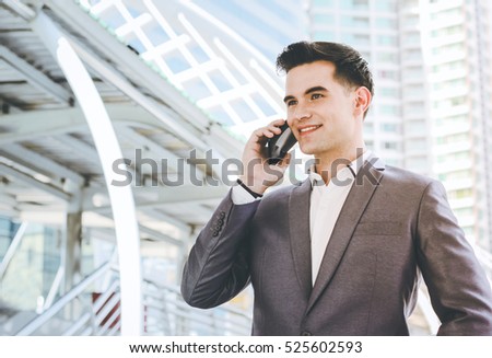 Smart young businessman smiling and talking on phone at sidewalk of the modern building