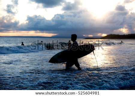 Surfing Themed Photos, an unrecognizable young man walking into the sea with a surf board.