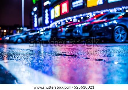 Rainy night in the parking shopping mall, parked cars illuminated advertising signs. Close up view from the level of the dividing line, image in the blue tones