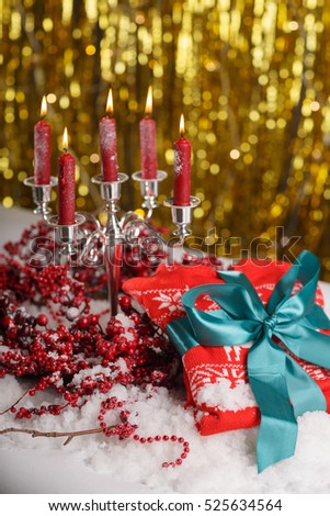 Christmas table decorations with burning candles in vintage candlestick  and wreath of  red berries in the snow over golden background. Warm woolen mittens with ribbon on the Christmas holiday table.
