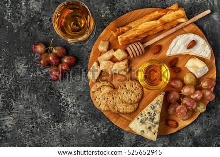 Assortment of cheese with wine, honey, nuts and grape on a cutting board, top view.