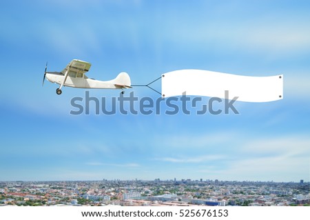 Vintage airplane fly and show advertising banner board on sky of town.  White poster for add message.