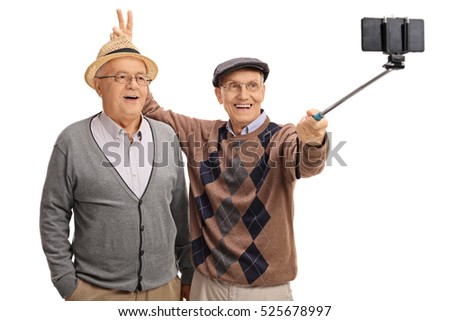 Elderly man pranking another man with bunny ears and taking a selfie with a stick isolated on white background