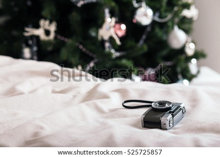 Vintage camera on soft white plaid cover with christmas tree at background.