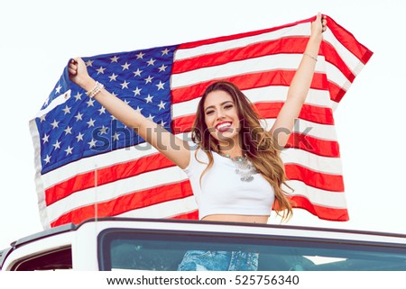 Happy Young Girl Standing In Convertible Car Holding Waving American USA Flag For Independence Day. Selective Focus.