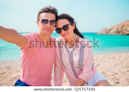 Selfie couple taking pictures on the beach in Cyclades. Tourists people taking travel photos with smartphone on summer holidays.