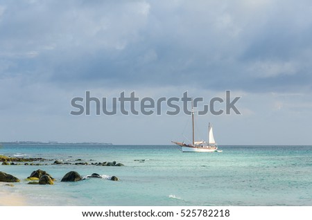 Picture showing a big sailboat on sea navigating towards the beach. The image was taken from Arashi Beach, Aruba, in the Caribbean Sea.