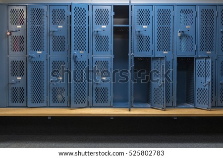 Blue metal cage lockers with a wood bench in a locker room with some doors open and some doors closed Royalty-Free Stock Photo #525802783