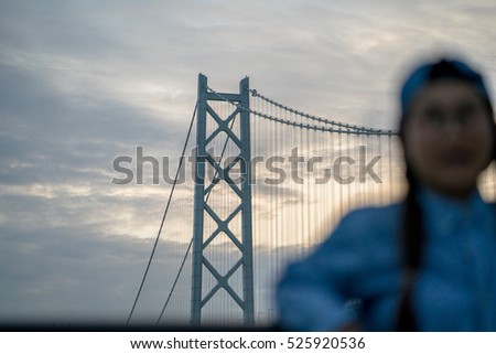 Blur Young pretty Asian girl wear blue jean shirt and cap posing on Akashi Kaikyo Bridge sunset   at Kobe , Japan.