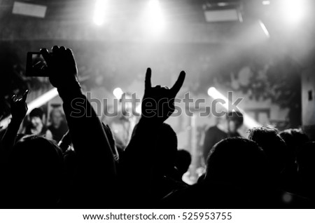 Silhouettes of people in a bright in the pop rock concert in front of the stage. Hands with gesture Horns. That rocks. Party in a club
