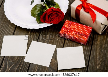White empty cards lie before present boxes and dinner plate with red rose