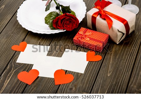 White empty cards lie before present boxes and dinner plate with red rose