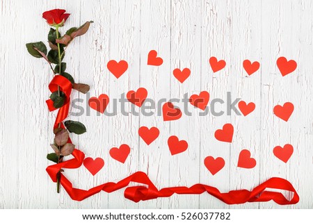 Red rose and paper hearts lie on white wooden table