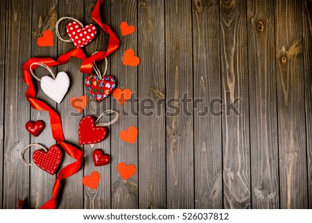 Red cloth and paper hearts with red ribbon lie on wooden table