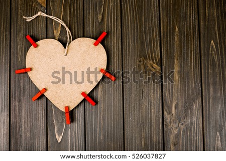 Wooden heart with red clothes pegs lies on wooden dinner table