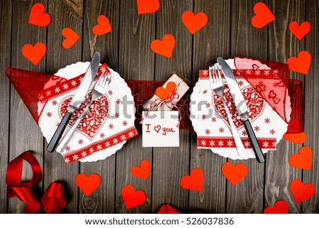 Festive dressed dinner plates lie on red ribbon among red paper hearts on wooden dinner table