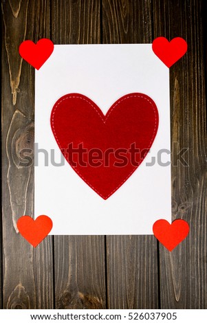 Large red cloth heart lies on white card on wooden table
