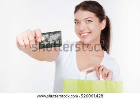 Picture of happy young woman dressed in white t-shirt holding purchasings and credit card after shopping. Isolated over white background. Look at camera. Focus on credit card.