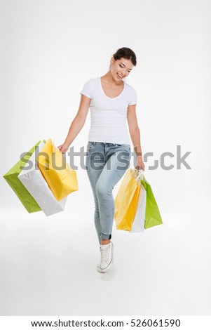 Picture of smiling woman holding purchasings after shopping. Isolated over white background. Looking down.
