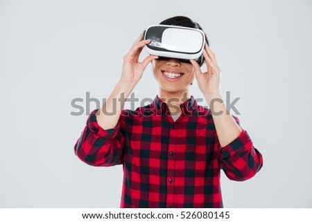 Photo of happy young asian man dressed in casual shirt in a cage and wearing virtual reality device. Isolated over white background.
