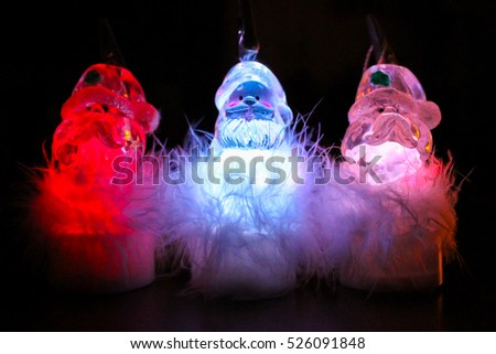 Three Luminous Santa Claus Toys standing on Dark Background
