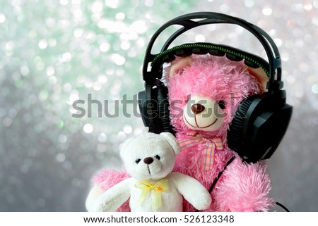 A big pink bear listening to the music by headphone and a little white bear on abstract picture of silver color Christmas powder for background, greeting cards, happiness festival, New years wishes