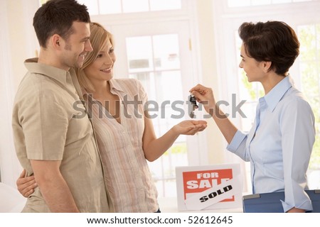 Estate agent handing over keys of new house to smiling couple.